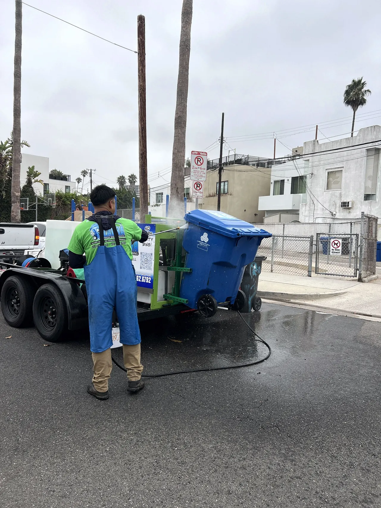 Zafra crew member pressure washing a blue recycling bin at the curb